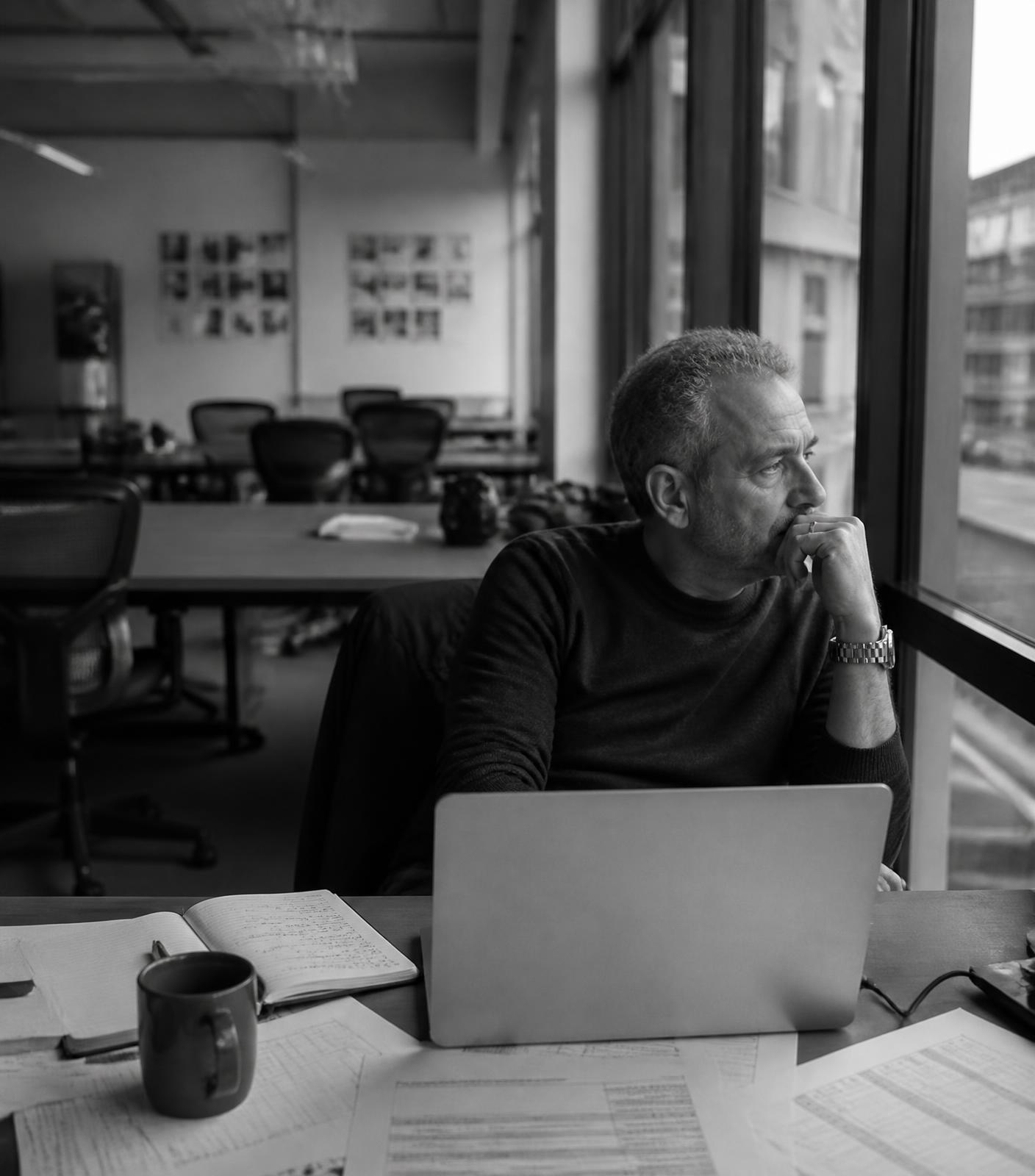 A founder alone at his desk, looking out of the window of an empty office